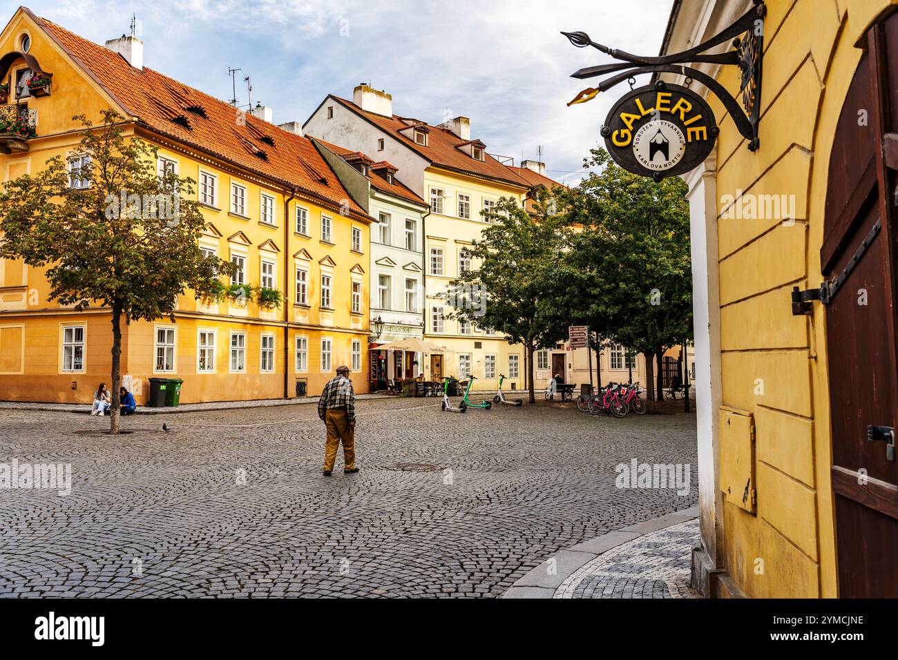 Glimpse of Na Kampe street in Kampa island, near Charles Bridge, with artistic shop sign and an old man walking, Mala Strana district, Prague, Czechia Stock Photo