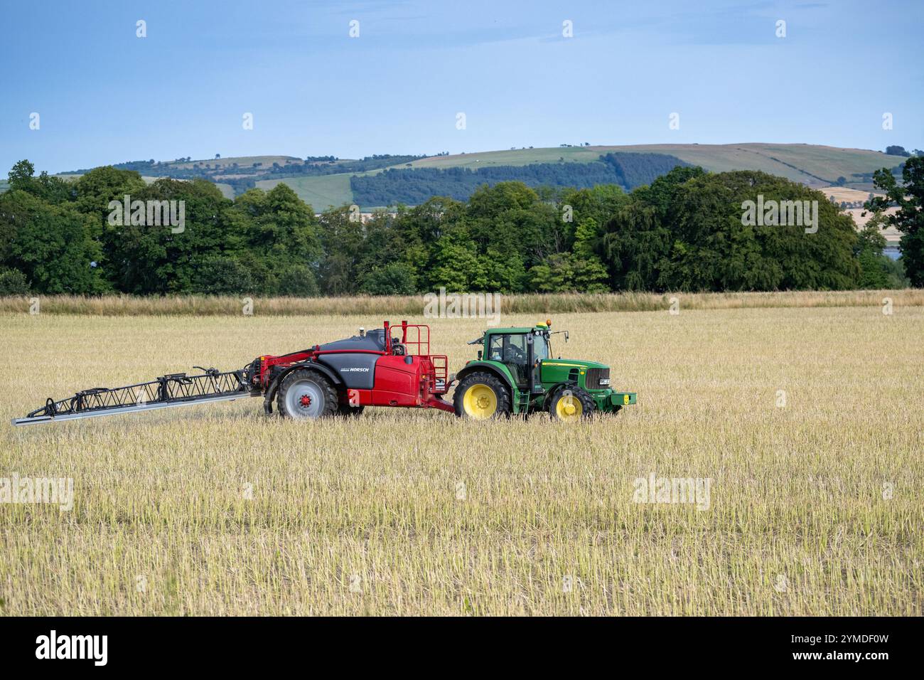 Farmer spraying an arable crop with a tractor and trailed sprayer overlooking the Cromartay Bay near Dingwall, Scotland, UK. Stock Photo