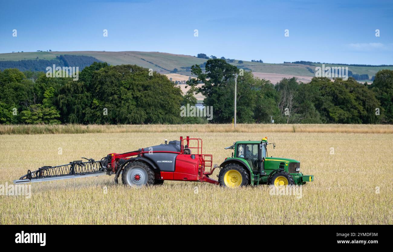 Farmer spraying an arable crop with a tractor and trailed sprayer overlooking the Cromartay Bay near Dingwall, Scotland, UK. Stock Photo