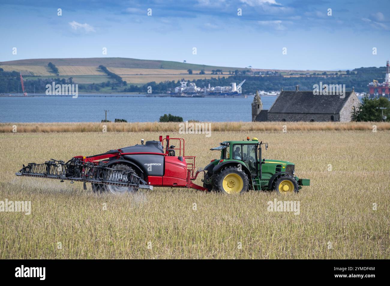 Farmer spraying an arable crop with a tractor and trailed sprayer overlooking the Cromartay Bay near Dingwall, Scotland, UK. Stock Photo