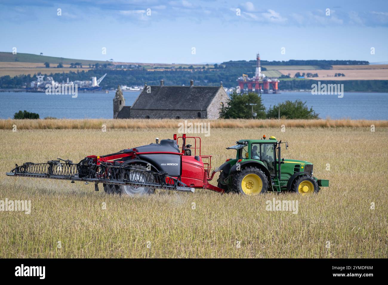 Farmer spraying an arable crop with a tractor and trailed sprayer overlooking the Cromartay Bay near Dingwall, Scotland, UK. Stock Photo