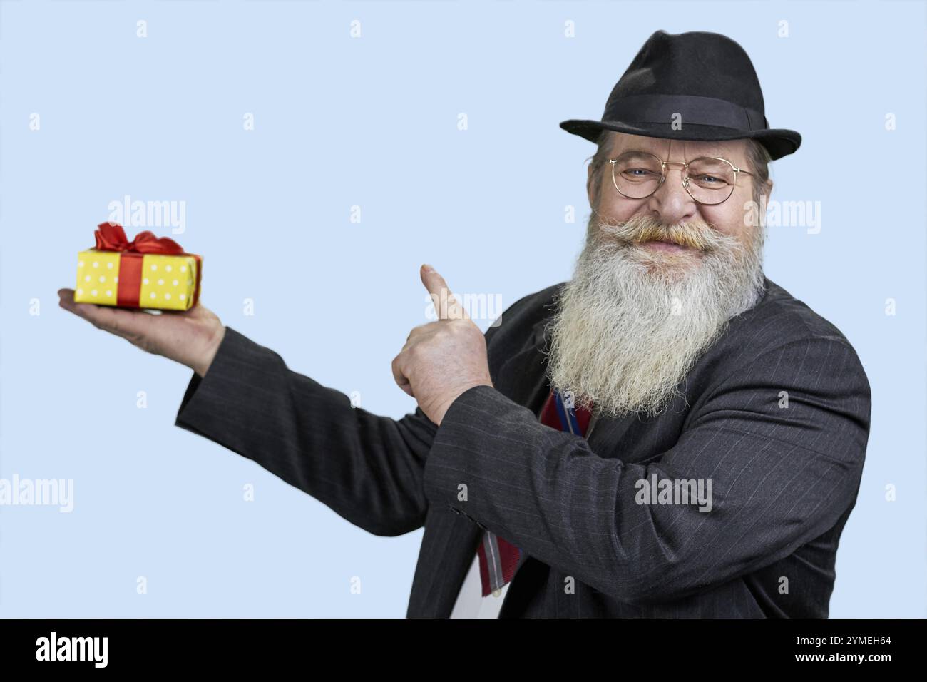 Happy senior bearded man pointing at gift box in another hand. Isolated on blue Stock Photo