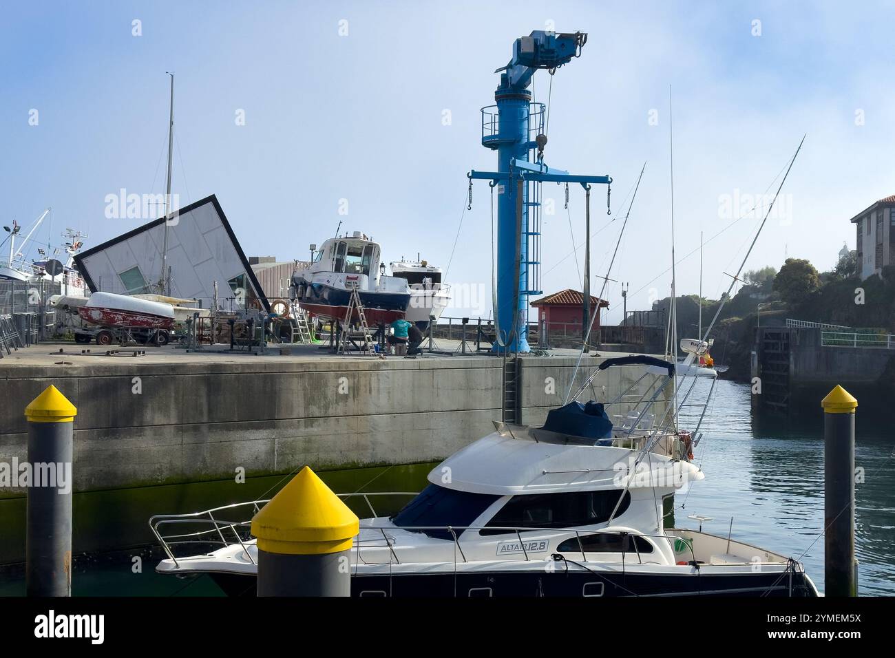 Two people fixing a boat at the small shipyard at the entrance to the port of Llanes, Asturias, Spain - Smartphone Captured Stock Image