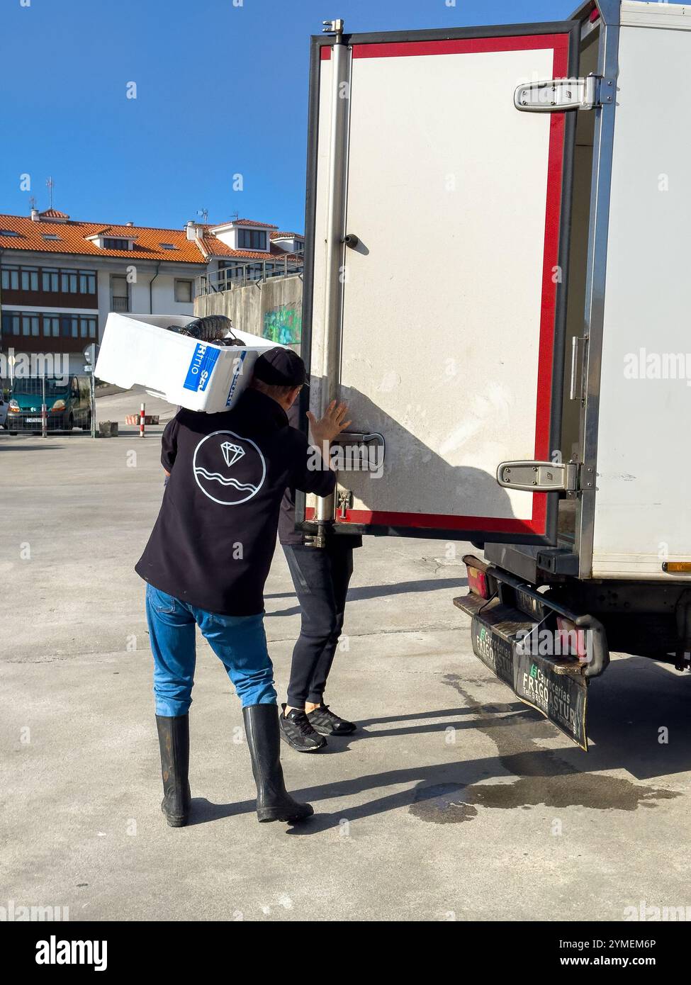 Two people are loading a large lobster onto a refrigerated truck in the port of Llanes, Asturias, Spain - Smartphone Captured Stock Image