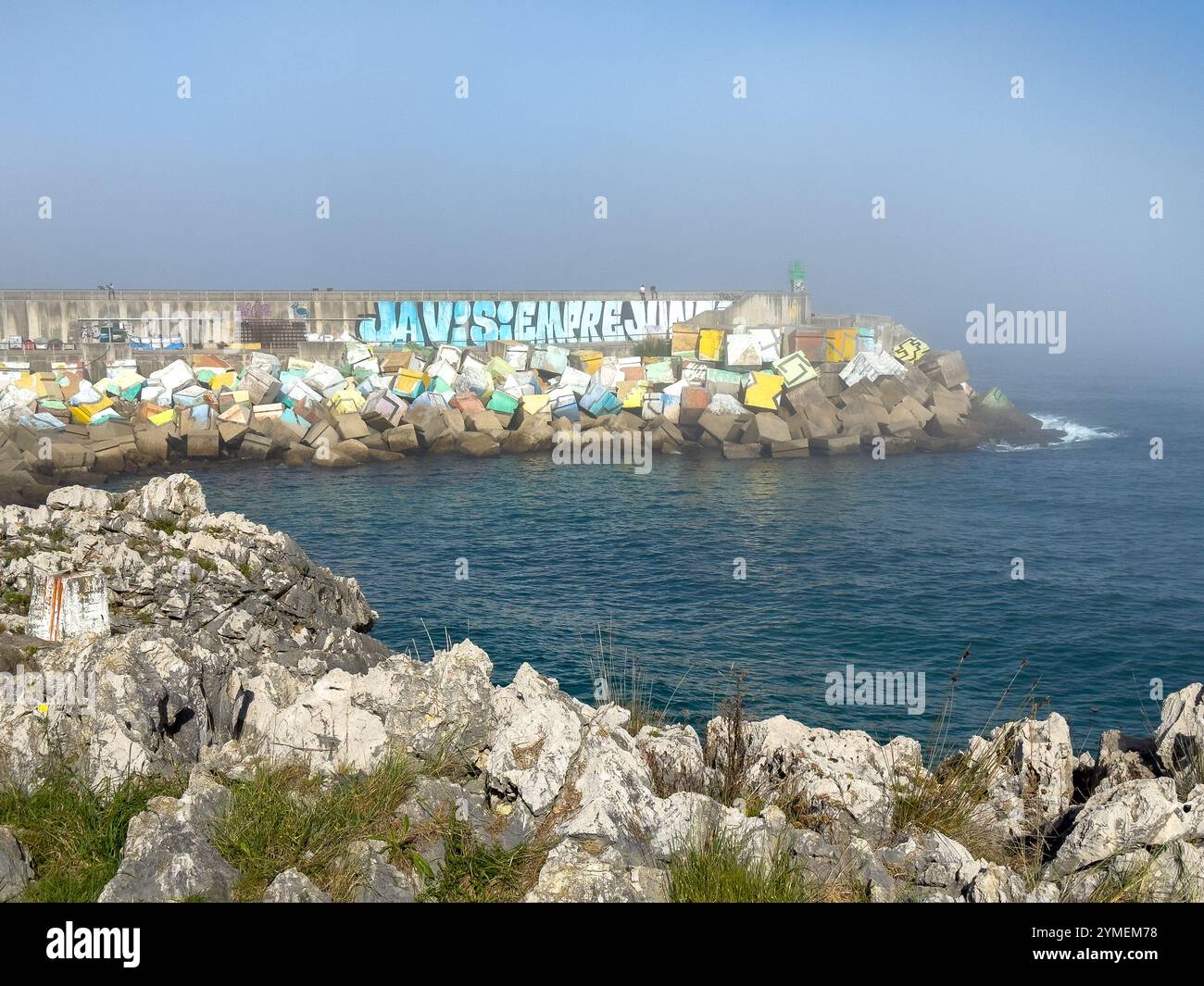 People sitting on the colorful breakwater on a misty day in Llanes, Asturias, Spain - Smartphone Captured Stock Image