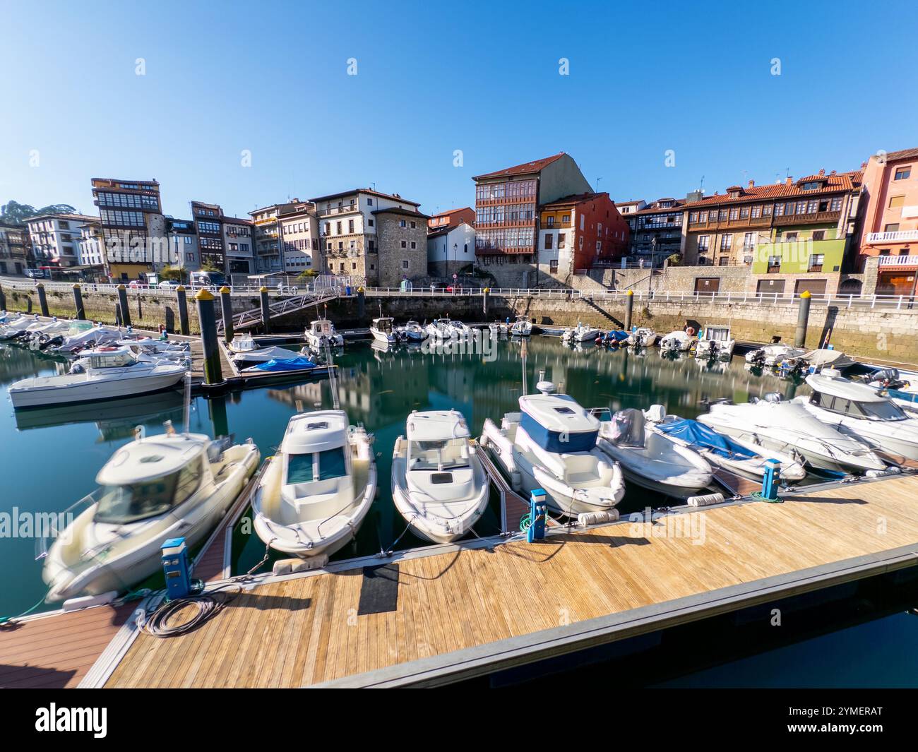 Moored yachts bobbing (long exposure shot) in the marina with some typical buildings of the old town of Llanes in the background, Asturias, Spain - Smartphone Captured Stock Image