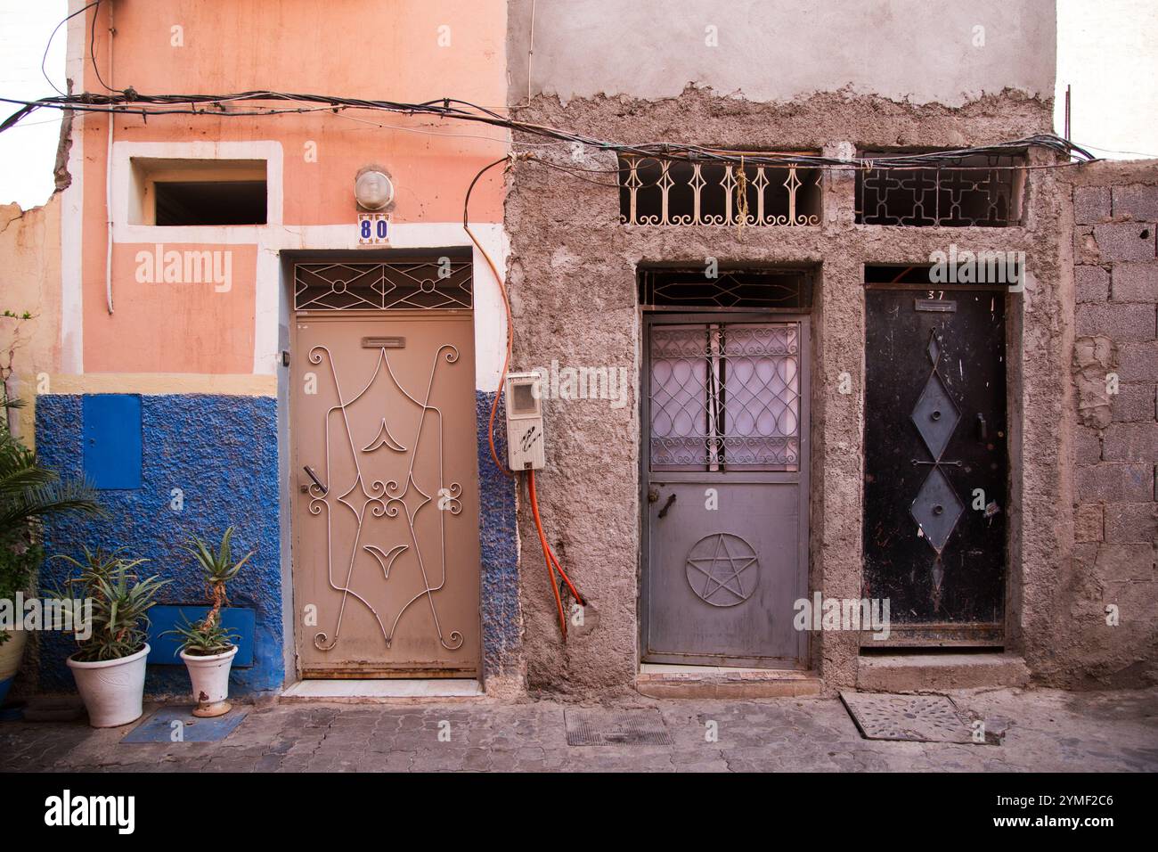 Colorful Marrakesh street scene with ornate doors, textured walls, vibrant paint, and potted plants, capturing Moroccan architecture and charm. Stock Photo