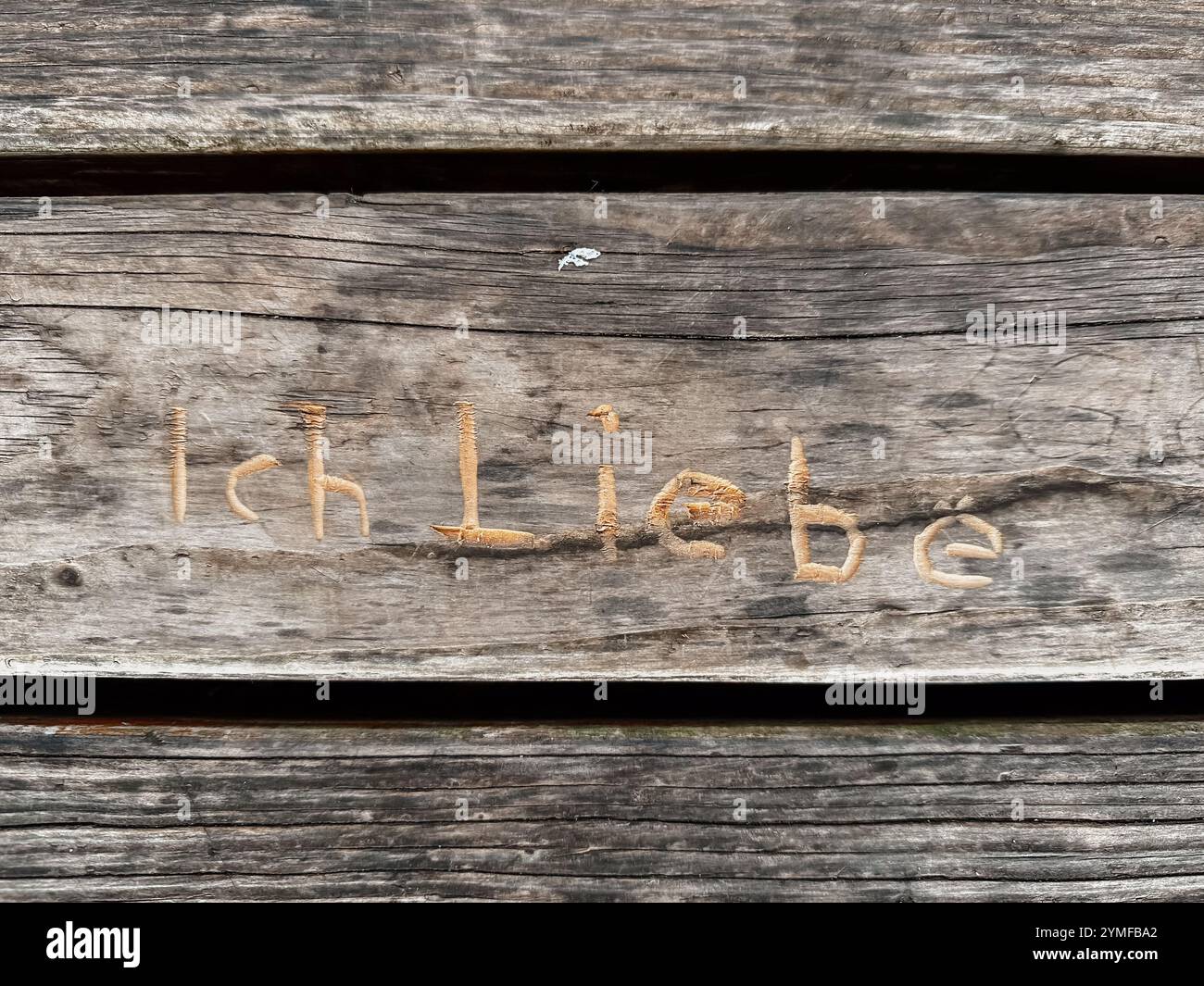 The wood is old and has a lot of scratches on it. The word Ich liebe is written on the wood in a cursive style Stock Photo