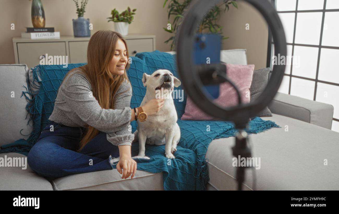 A young blonde woman and her pet dog sitting on a cozy couch in a ...