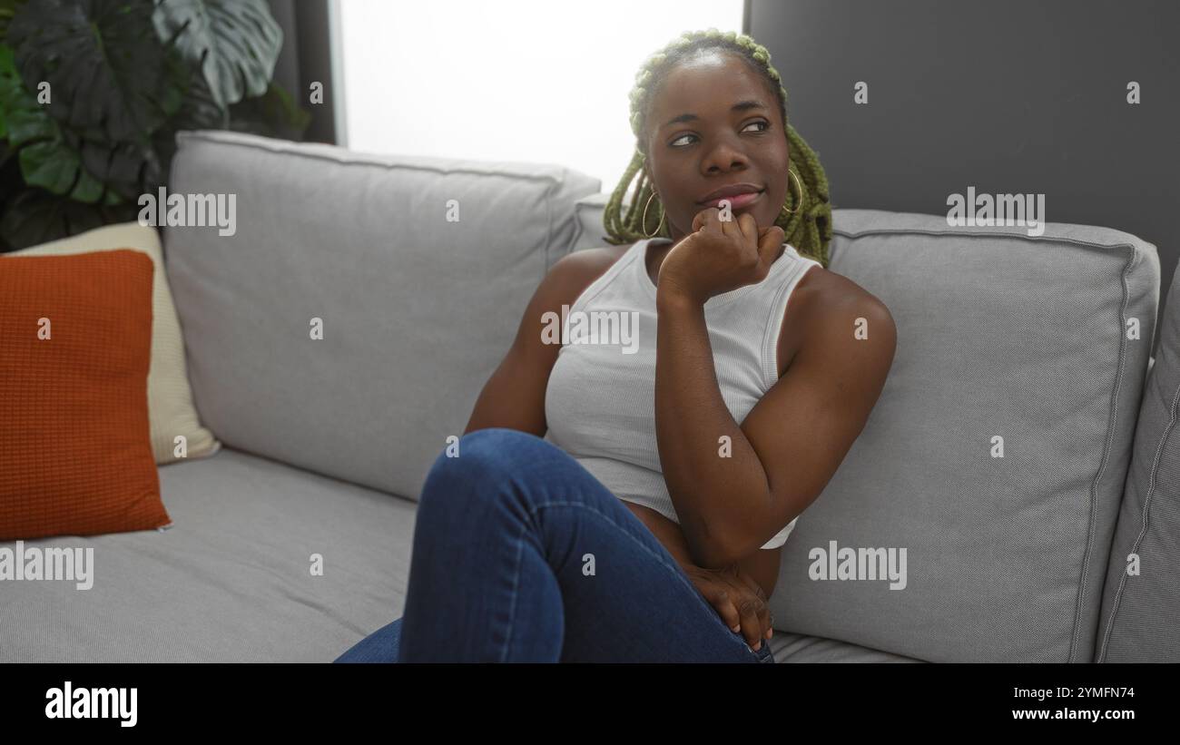 Young african american woman with braids sitting on a sofa in an indoor ...