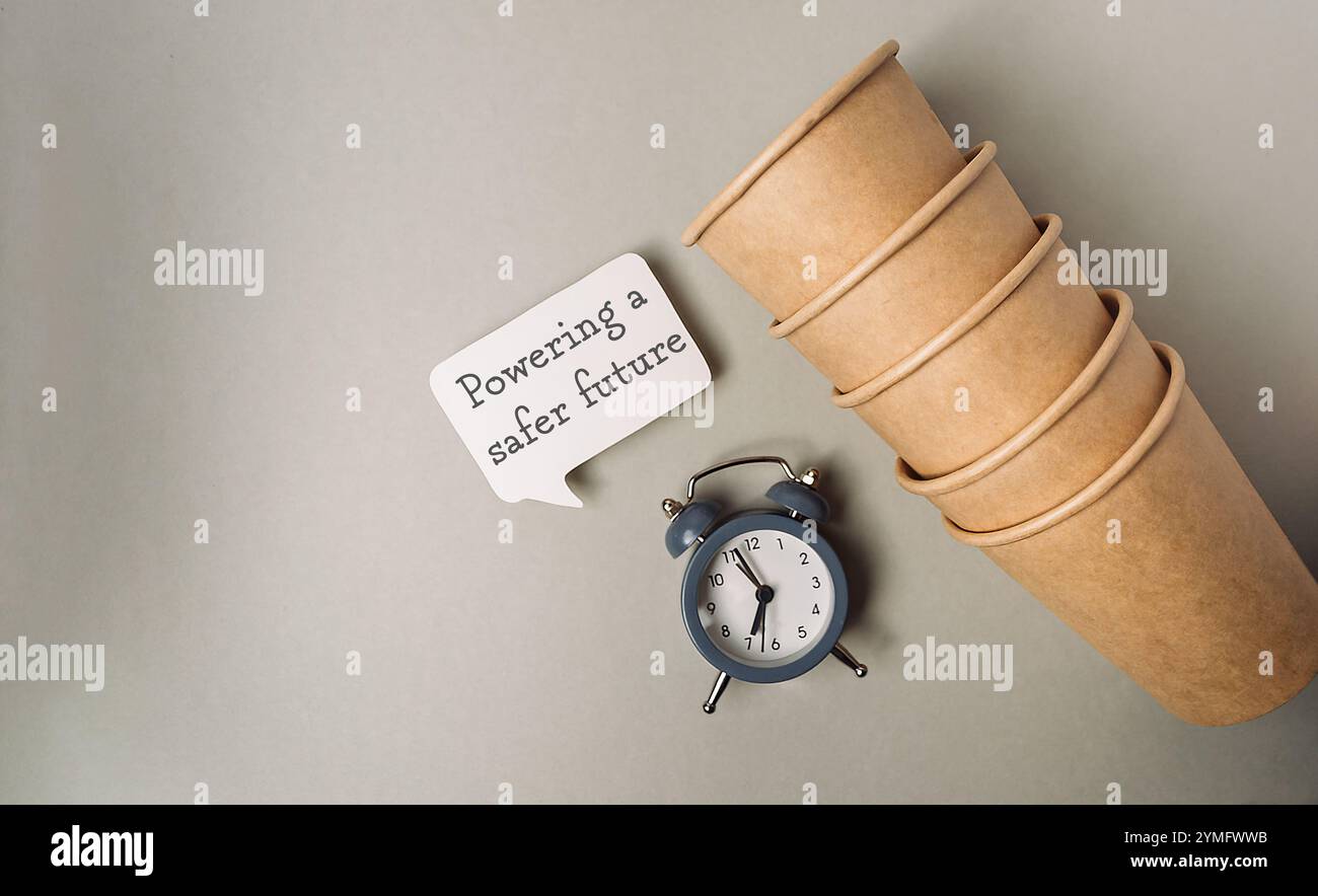 Clock sits on a table next to a stack of paper cups. The cups are ...