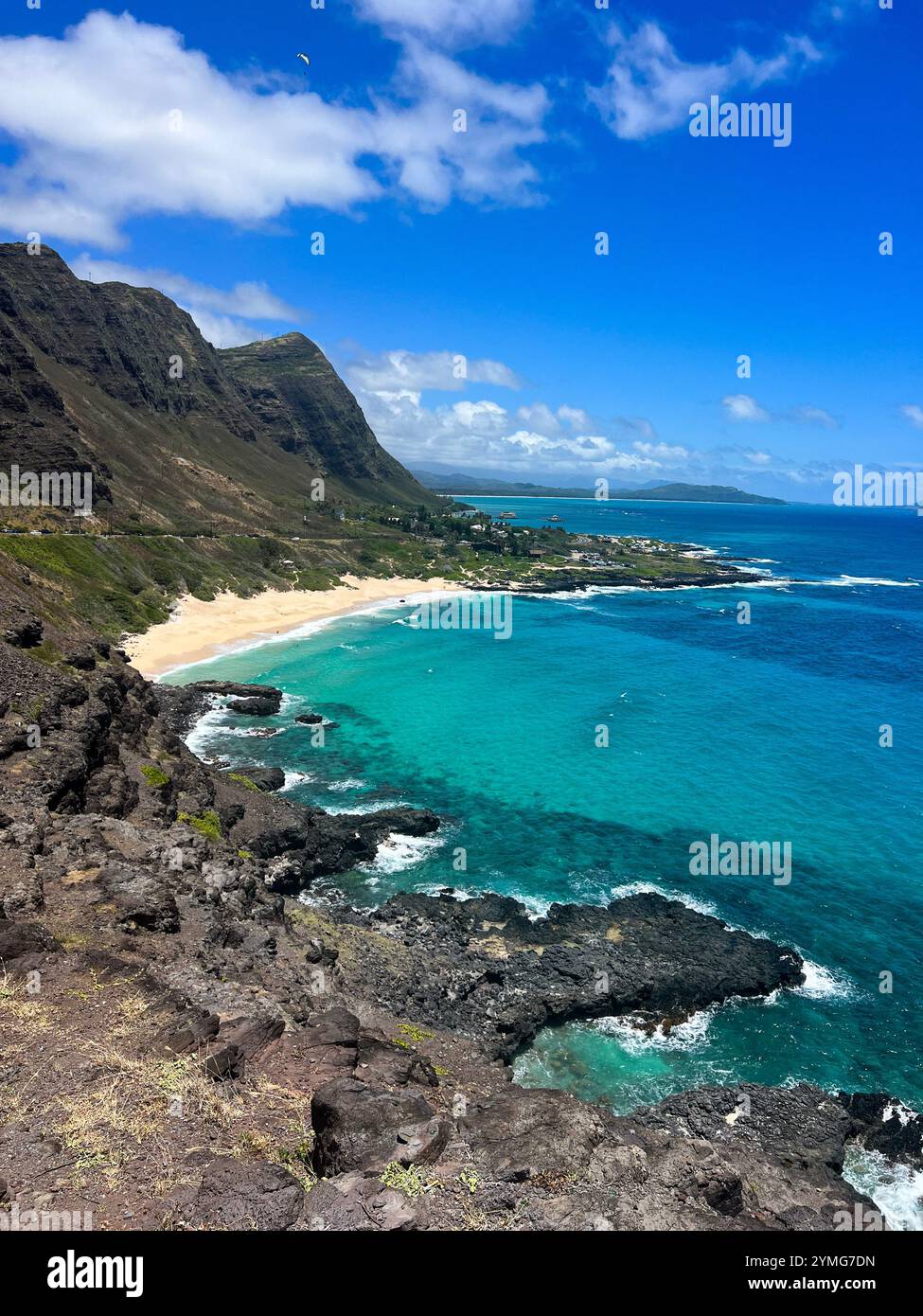 A stunning view from a clifftop overlooking a secluded cove with a sandy beach and crystal clear turquoise water. People are enjoying the beach - Smartphone Captured Stock Image