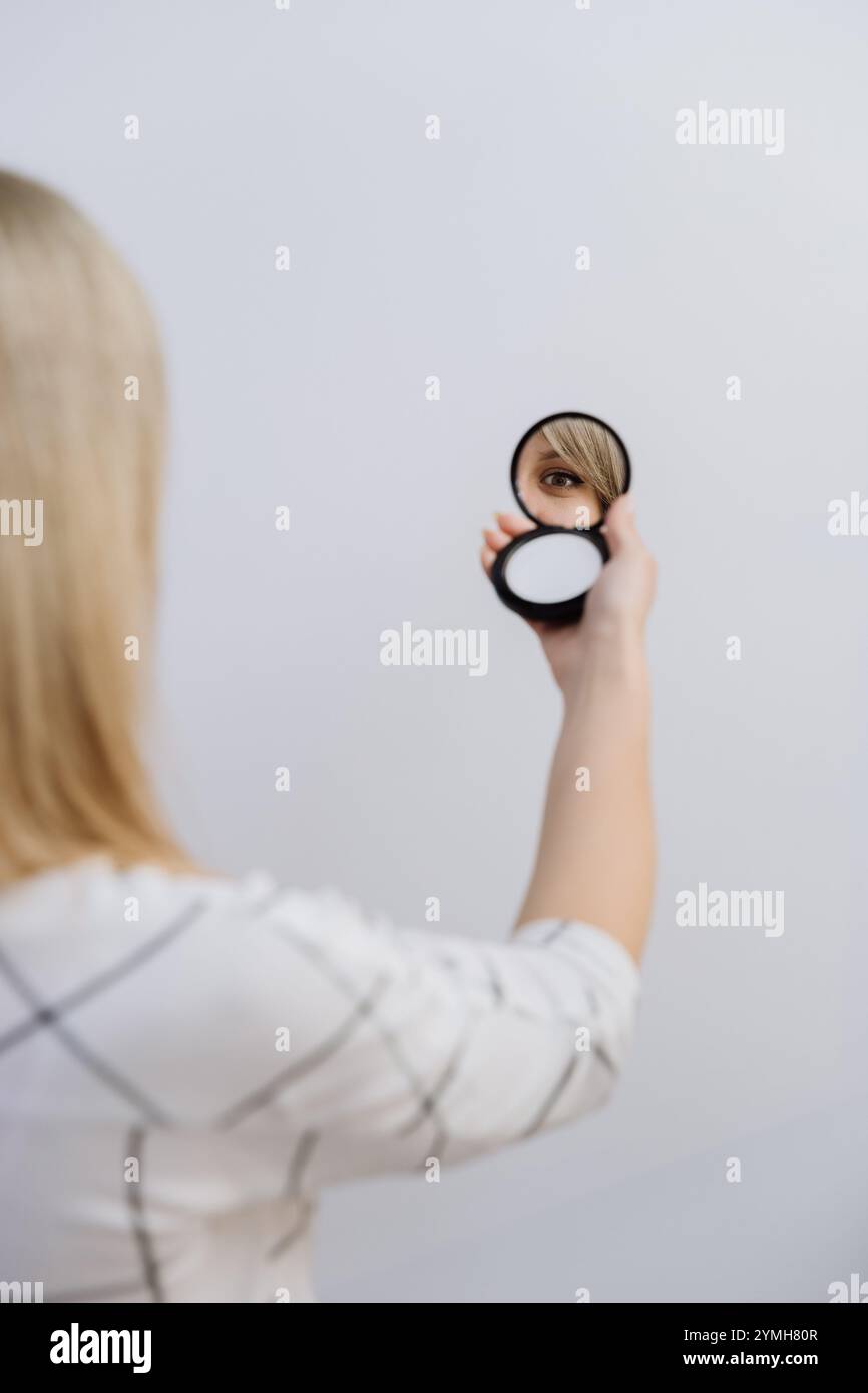 Reflection of a womans eye in a handheld compact mirror against a minimal background. Stock Photo