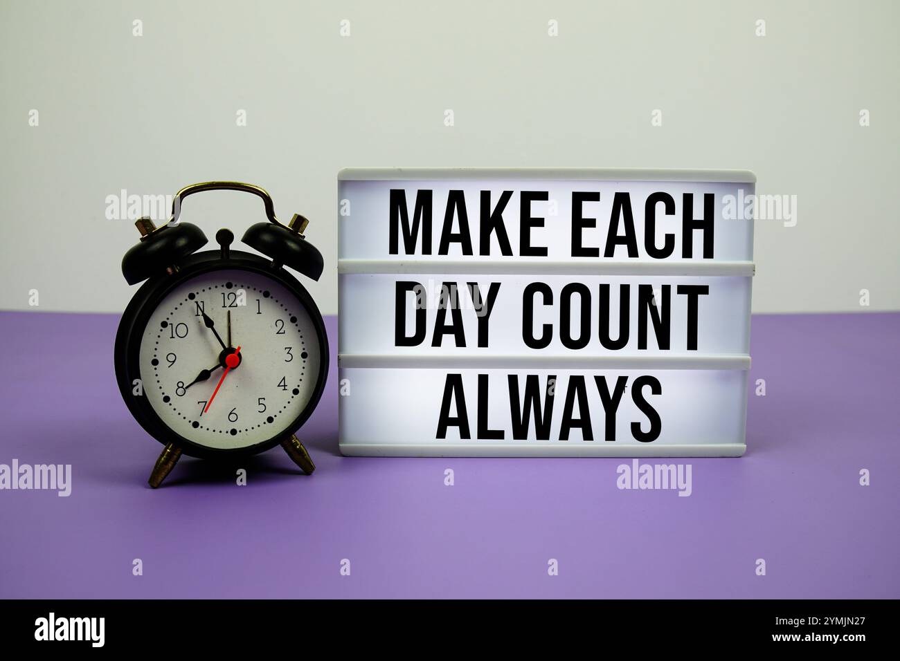 Make each day count always text on LED lightbox with alarm clock on purple background Stock Photo