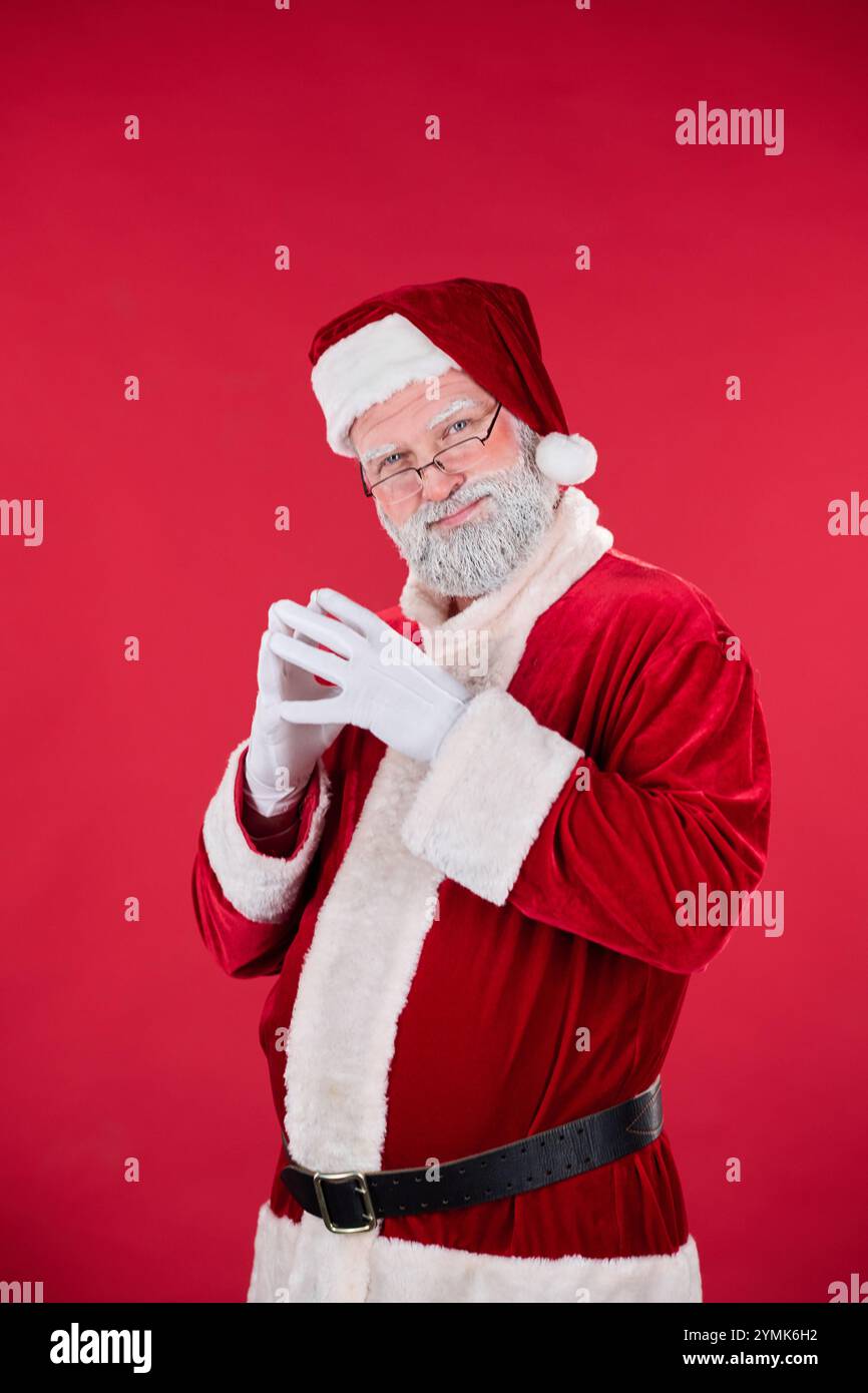 Santa Claus standing against bright red background, smiling while ...