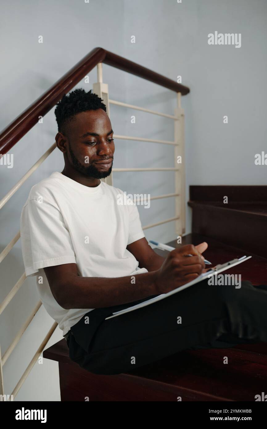 African American Man Writing Notes on Stairs Stock Photo