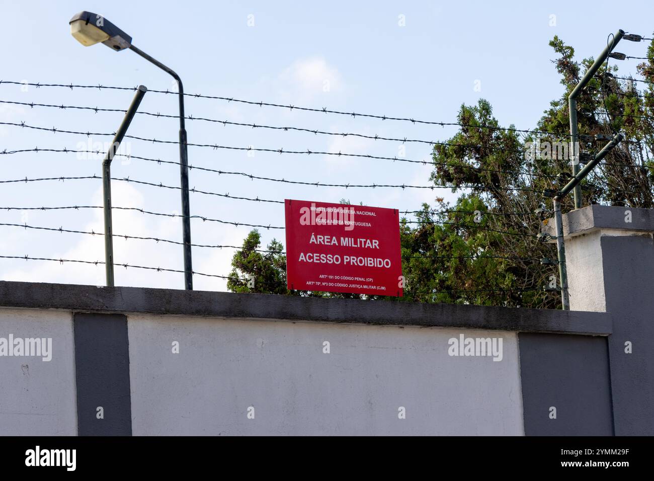 Barbed wire topping a perimeter wall with a no trespassing sign protecting a restricted military area Stock Photo