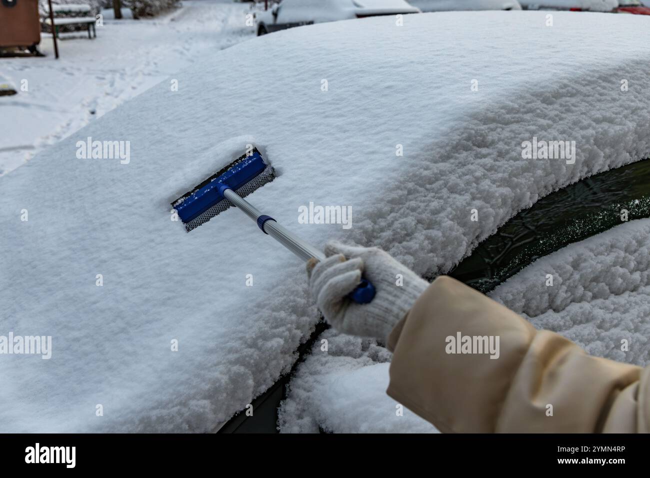 A woman shovels snow from the car, removing ice from the car body ...