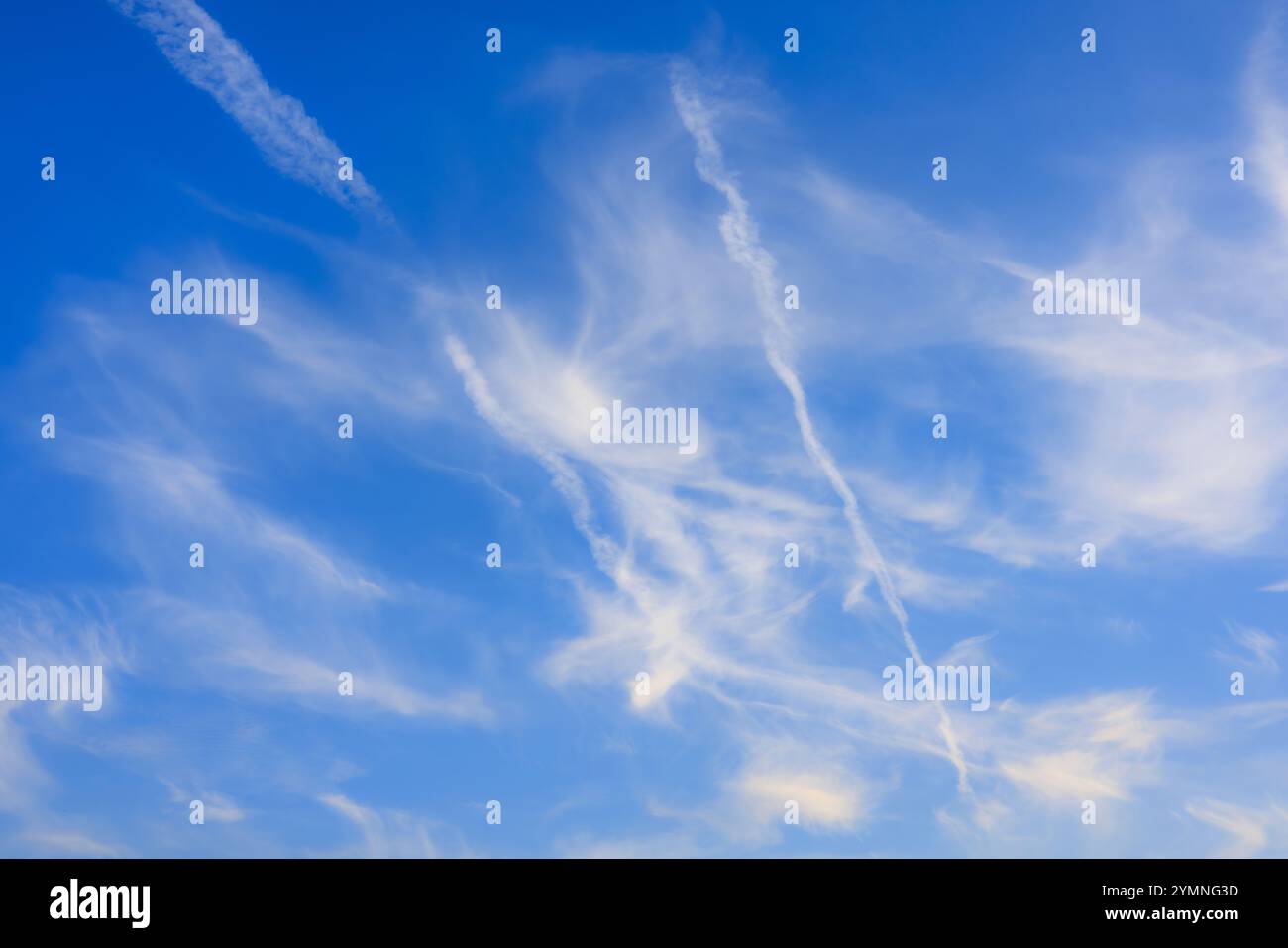 White cirrus clouds and contrails of planes crossing the sky. Bright blue background. Stock Photo