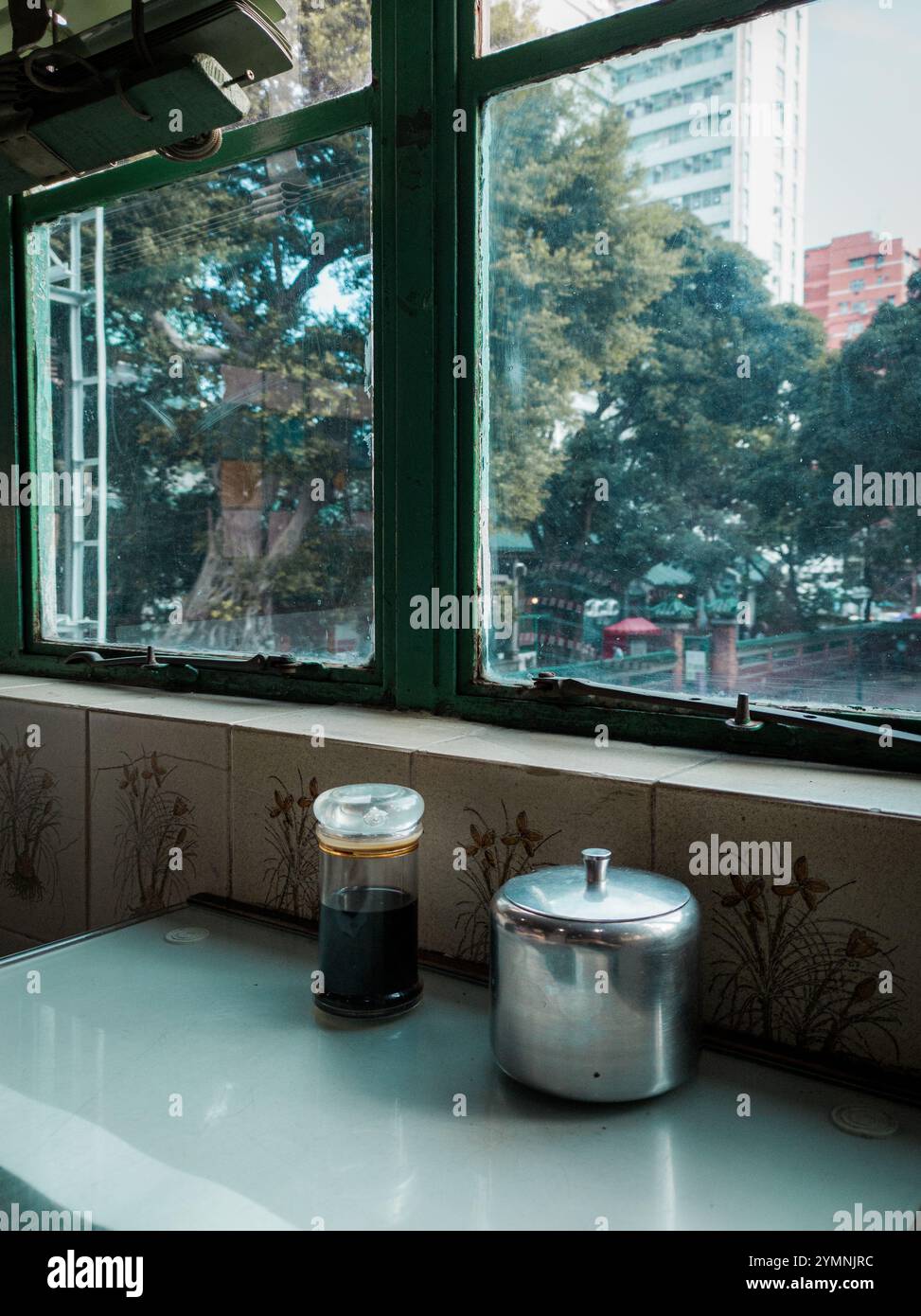 Vintage Hong Kong Café Interior with Condiment Bottles on Tiled Countertop and Scenic Window Overlooking Urban Greenery Stock Photo