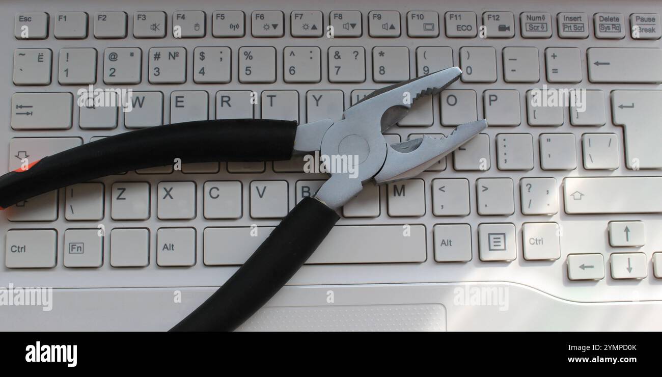 Pliers on a white computer keyboard with latin characters only stock photo. Computer Repairing Concept. Steel Pliers On Laptop Keyboard Stock Photo