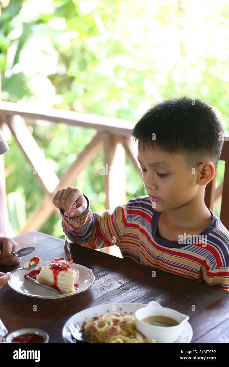 A young child sits at a wooden table, enjoying a delicious dessert topped with strawberries, surrounded by a bright, natural atmosphere. Stock Photo