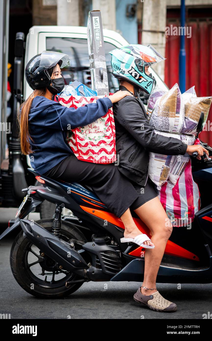 A Filipino woman carries her shopping on the back of a moped through the streets of Manila, The Philippines. Stock Photo