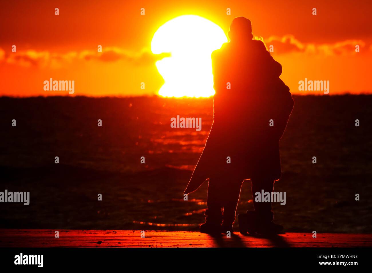 Isle Of Palms, United States. 23rd Nov, 2024. A couple, bundled up against the early morning chill are silhouetted by the sunrise, as they watch the sun rise over the Atlantic horizon on Front Beach, November 23, 2024 in Isle of Palms, South Carolina. A cold front swept down the Eastern United States dropping temperatures across the low country. Credit: Richard Ellis/Richard Ellis/Alamy Live News Stock Photo