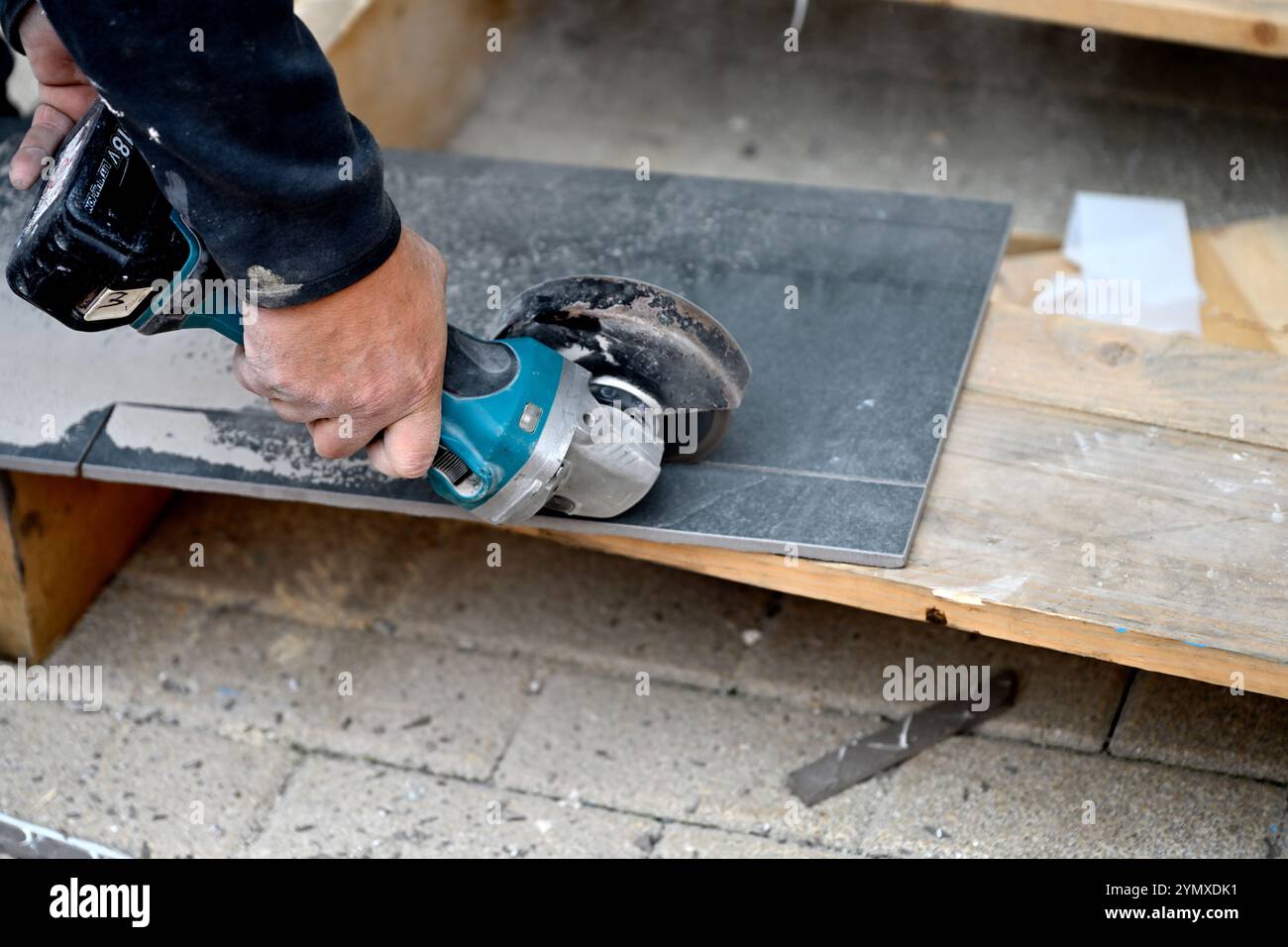 Man using battery powered angle grinder to cut ceramic floor tile Stock Photo
