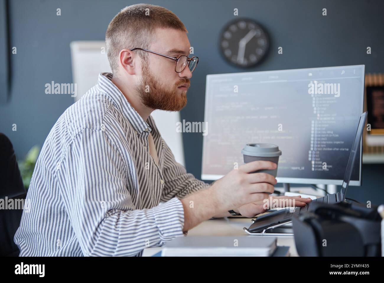 Young professional with beard coding on computer at office desk while ...