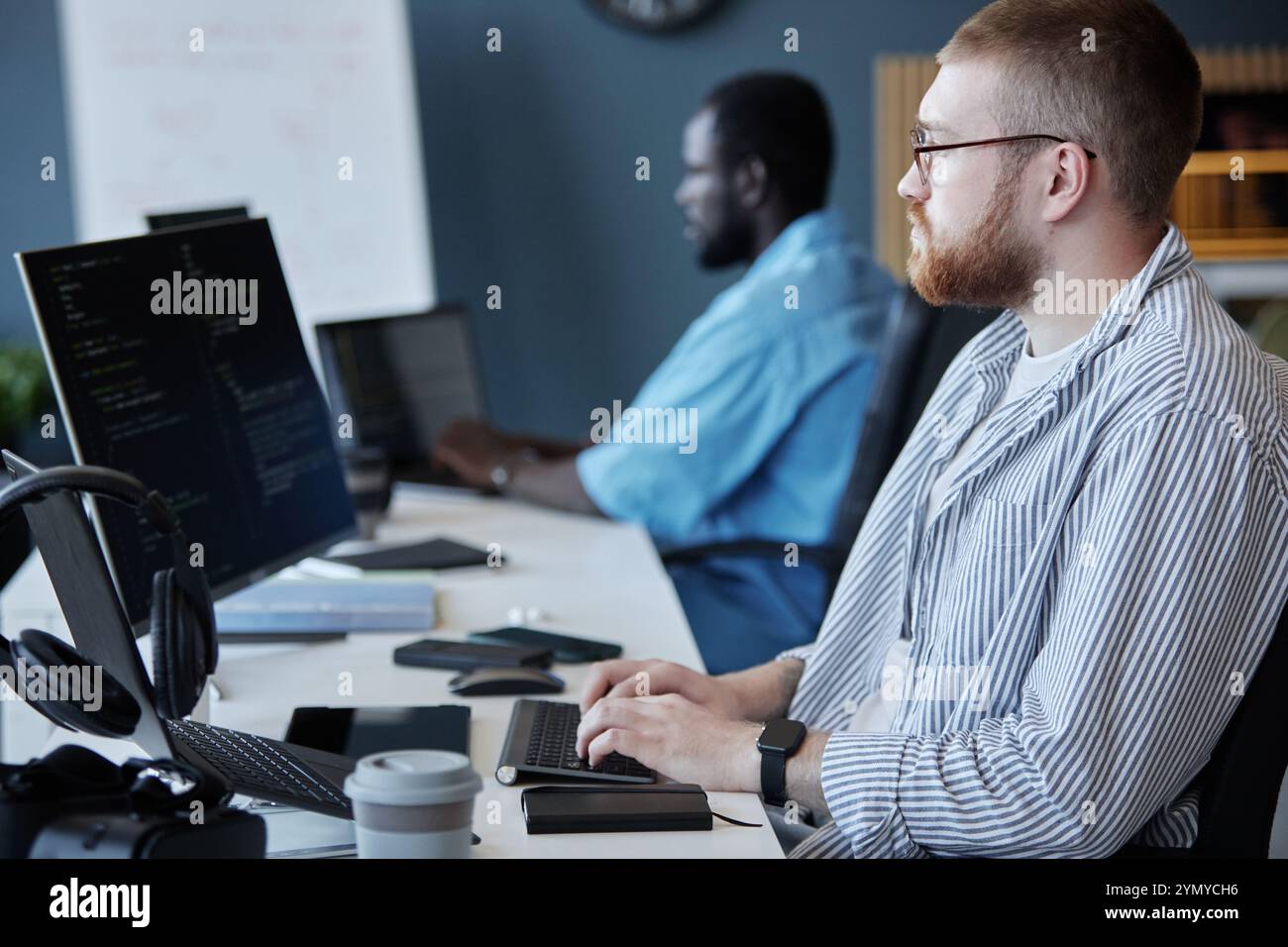 Multi-ethnic group of developers focused on coding and discussing project details in a modern office setting. Senior programmer working on computer sc Stock Photo