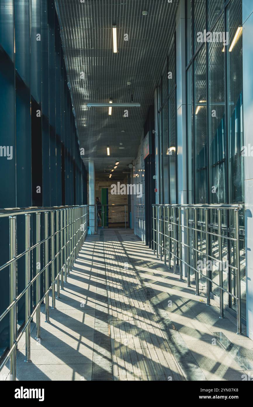 A sunlit corridor in a modern building featuring metal railings and ...