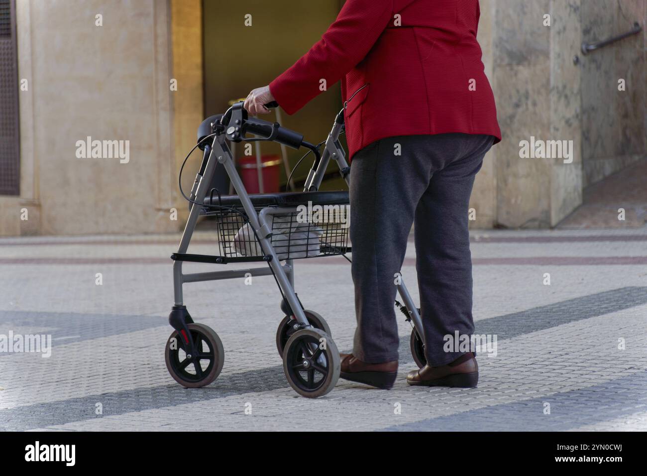 Elderly woman walking along a pedestrian street leaning on her wheeled ...