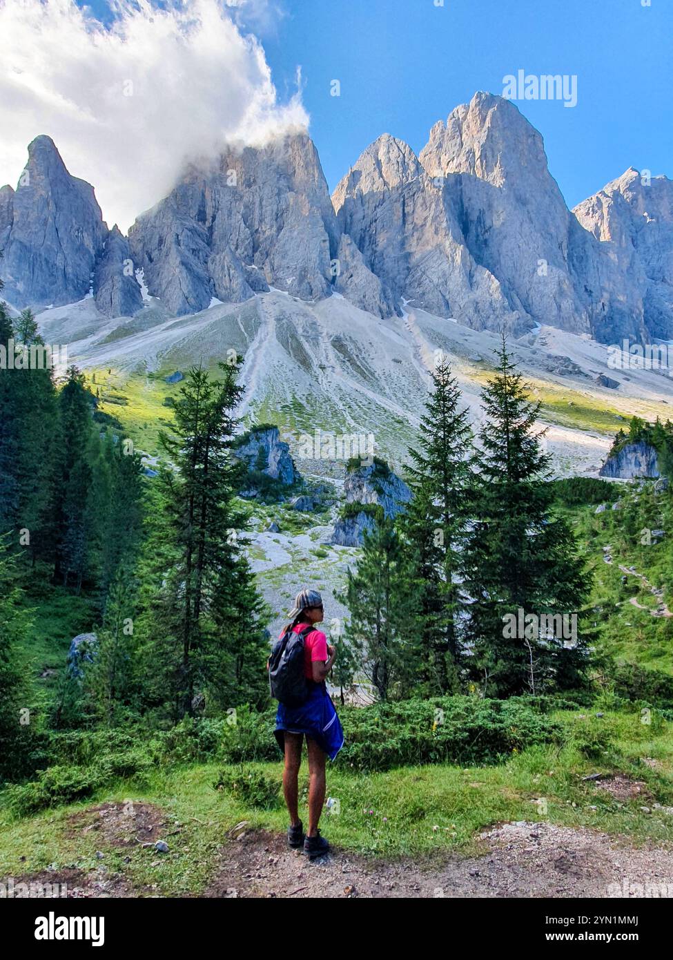 Beneath towering mountain ranges in the Dolomites, a hiker stands in ...