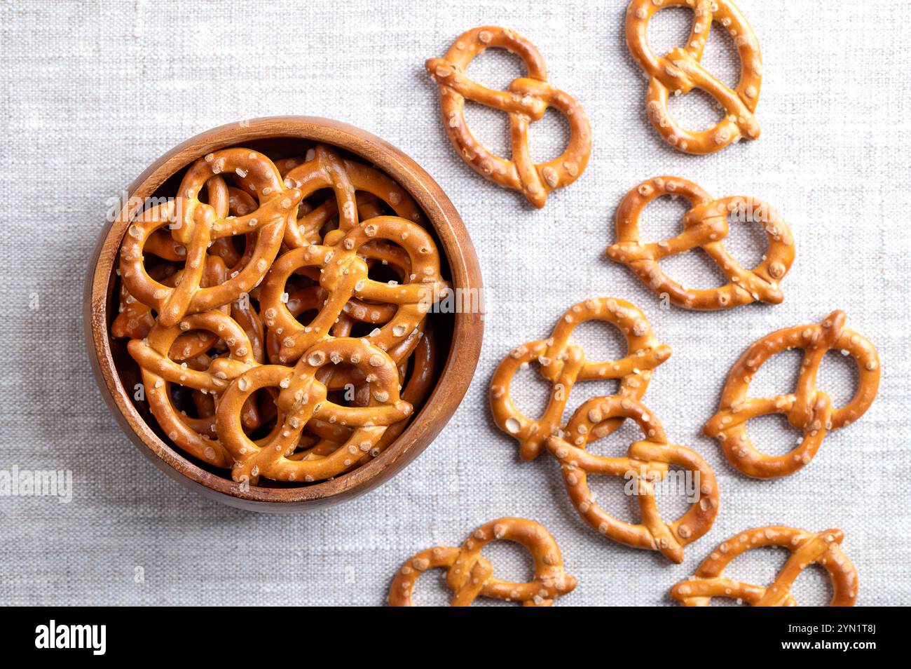Salted pretzels in a wooden bowl on linen fabric. Golden toasted small pretzels of traditional shape with ends intertwined to form a pretzel bow. Stock Photo