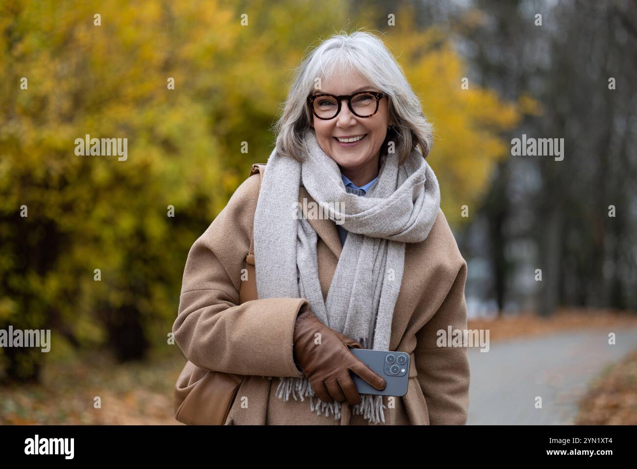 Smiling older woman in a stylish coat and scarf enjoying a walk in a ...