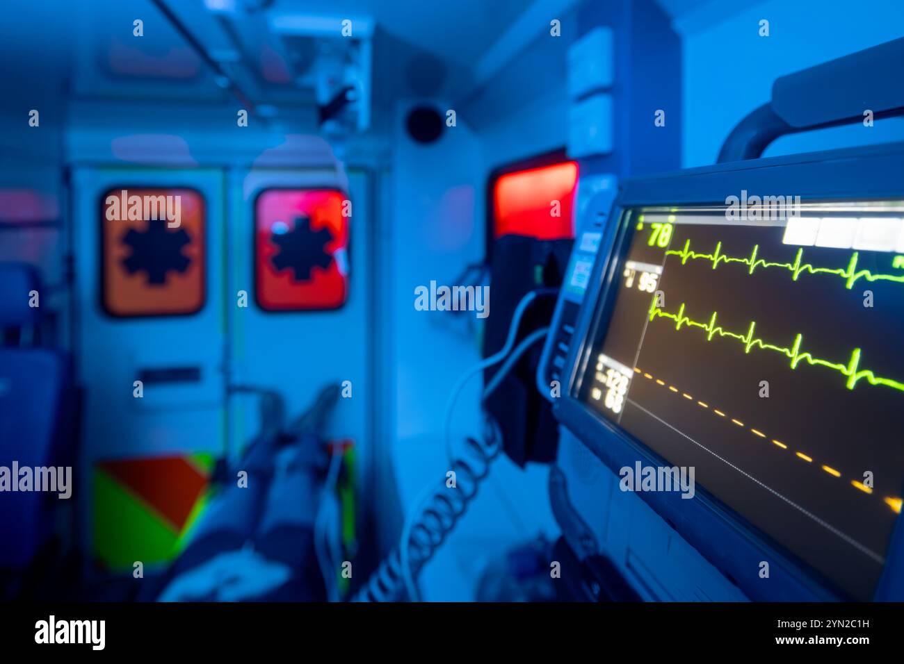 Selective focus on monitor of vital signs against patient on stretcher inside ambulance car of emergency medical service at night. Themes rescue, urge Stock Photo