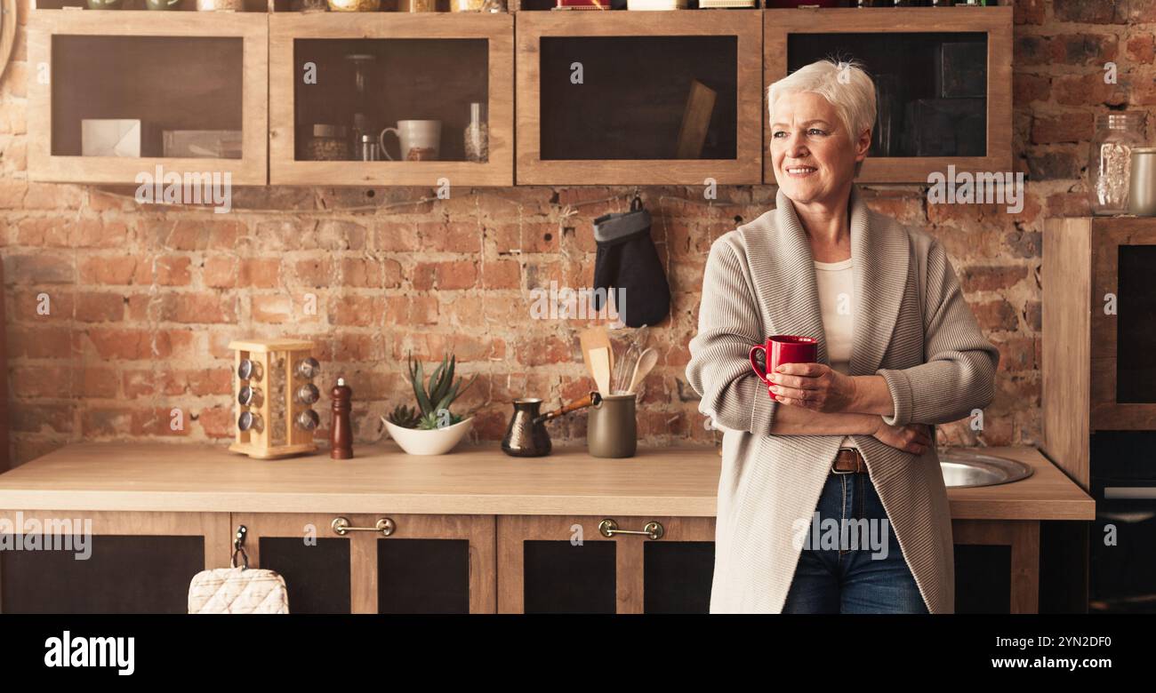Calm senior lady standing at kitchen, drinking coffee Stock Photo
