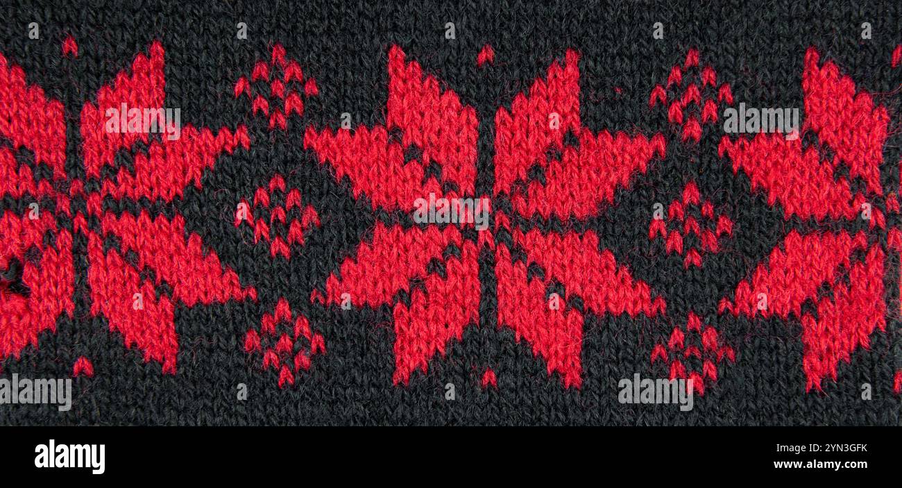 Red color eight pointed star knitted pattern on sweater. Red stars on black background, studio shot, indoors. Stock Photo
