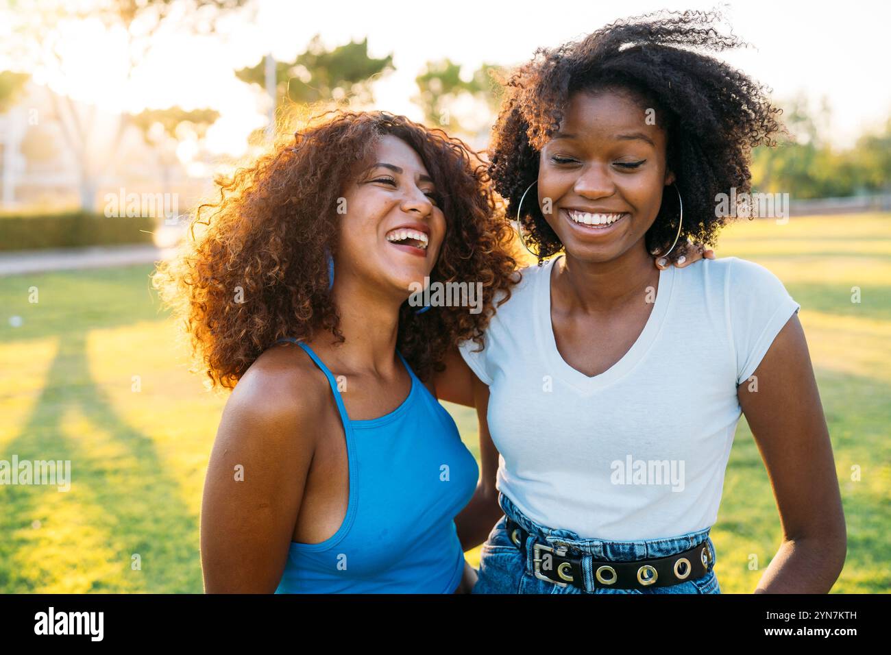 Two young women are laughing together in a sunny park Stock Photo - Alamy