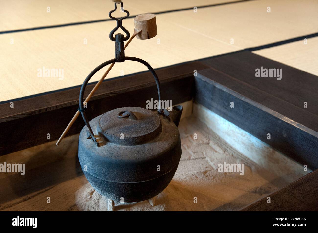 An iron tetsubin kettle hanging above an irori sunken fire pit hearth with a bamboo ladle in a traditional country home in Japan. Stock Photo