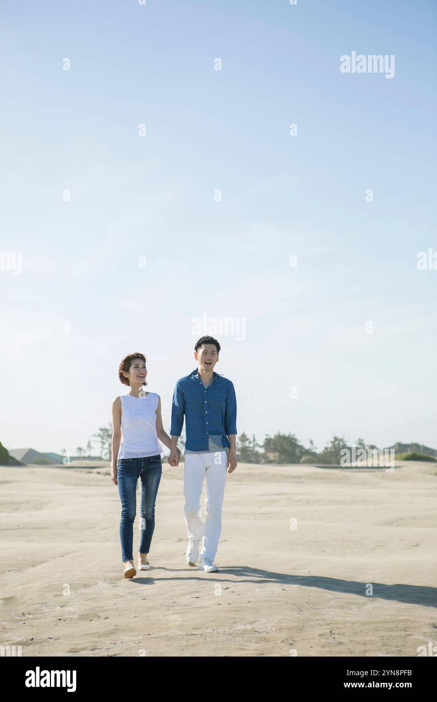 Couple in their 20s and 30s walking on sandy beach Stock Photo - Alamy