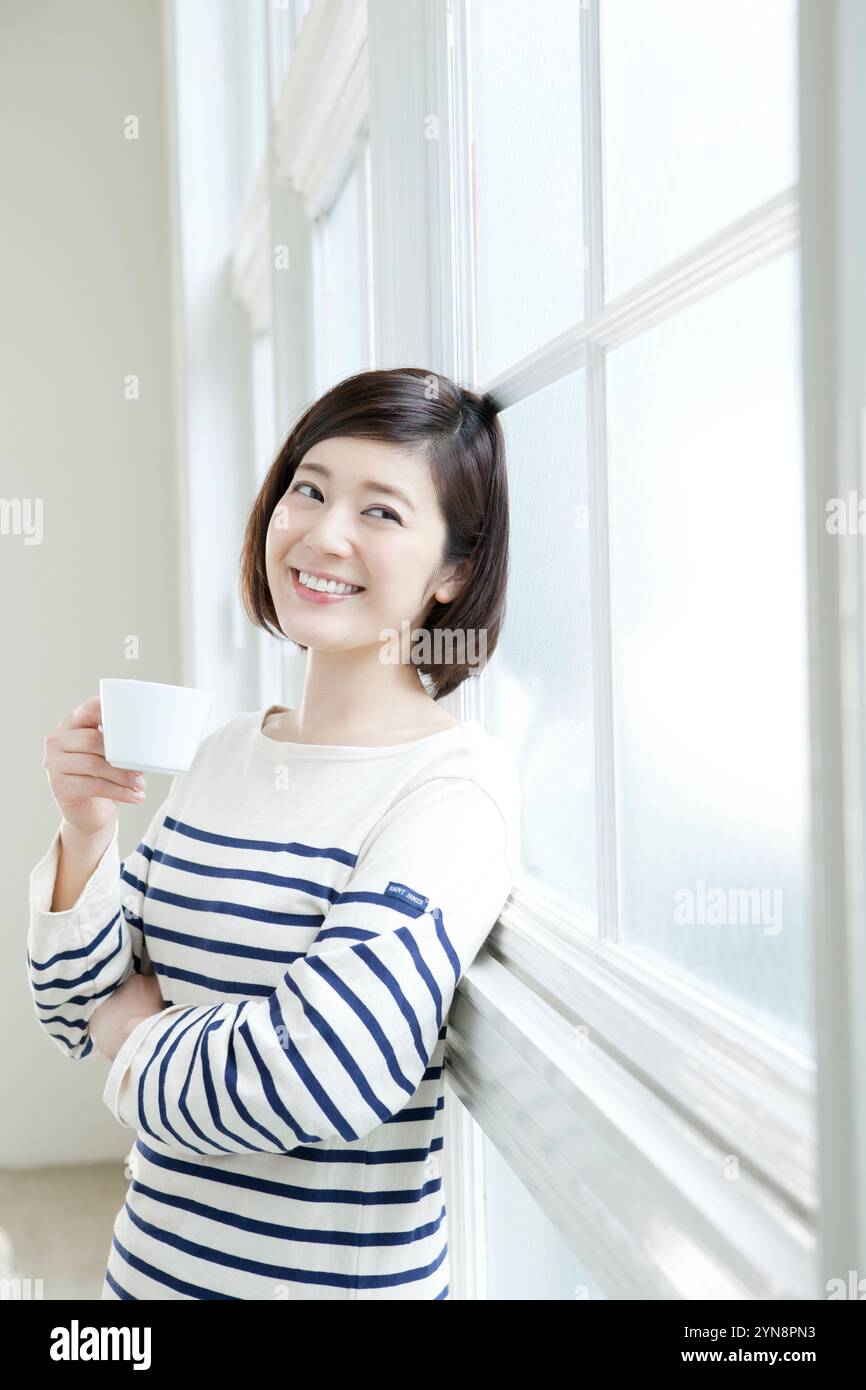 Woman in her 20s drinking coffee by the window Stock Photo - Alamy