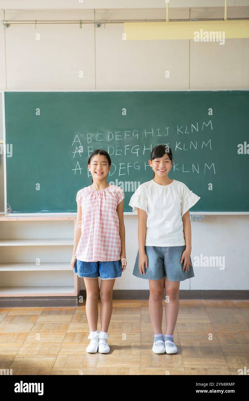Two smiling girls standing in a classroom Stock Photo - Alamy