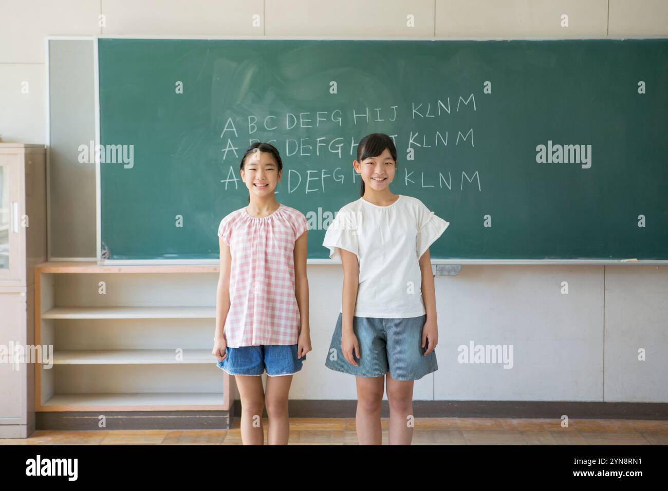 Two smiling girls standing in a classroom Stock Photo - Alamy