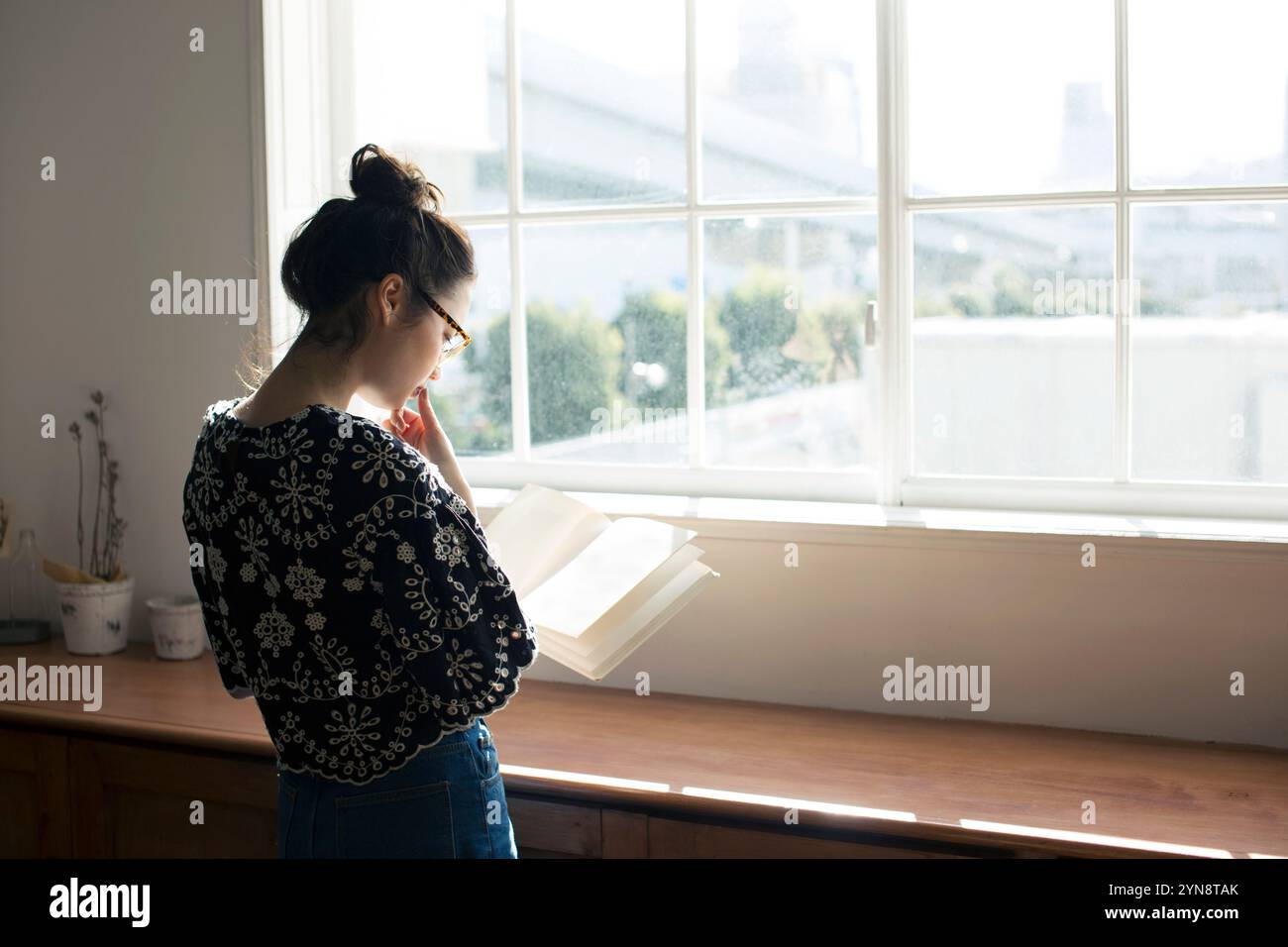Woman in her 20s reading a book by the window Stock Photo - Alamy