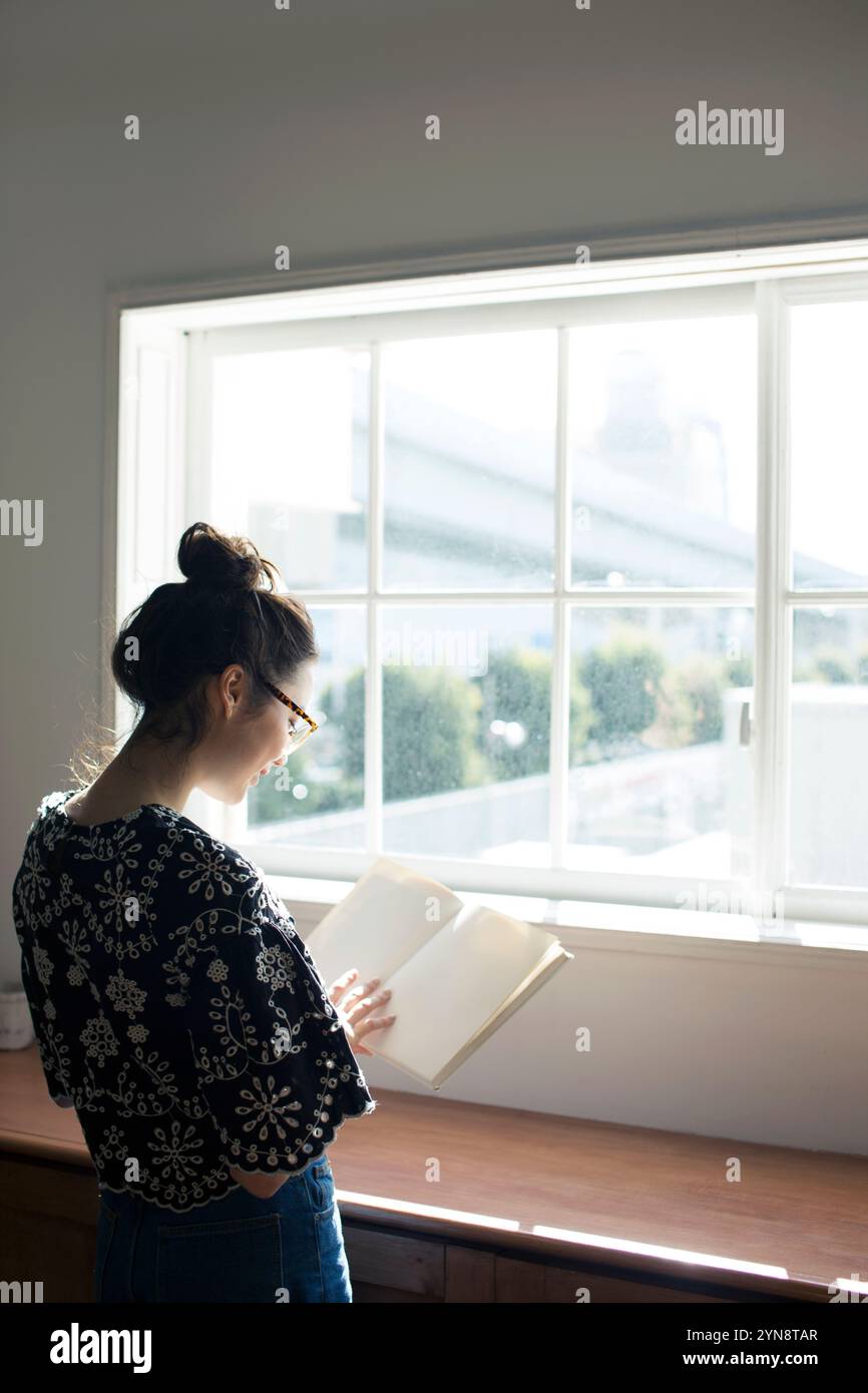 Woman in her 20s reading a book by the window Stock Photo - Alamy