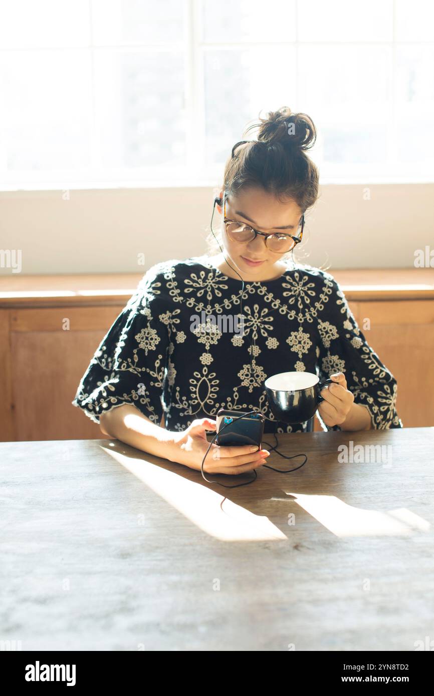 Woman in her 20s sitting by the window looking at her phone Stock Photo ...