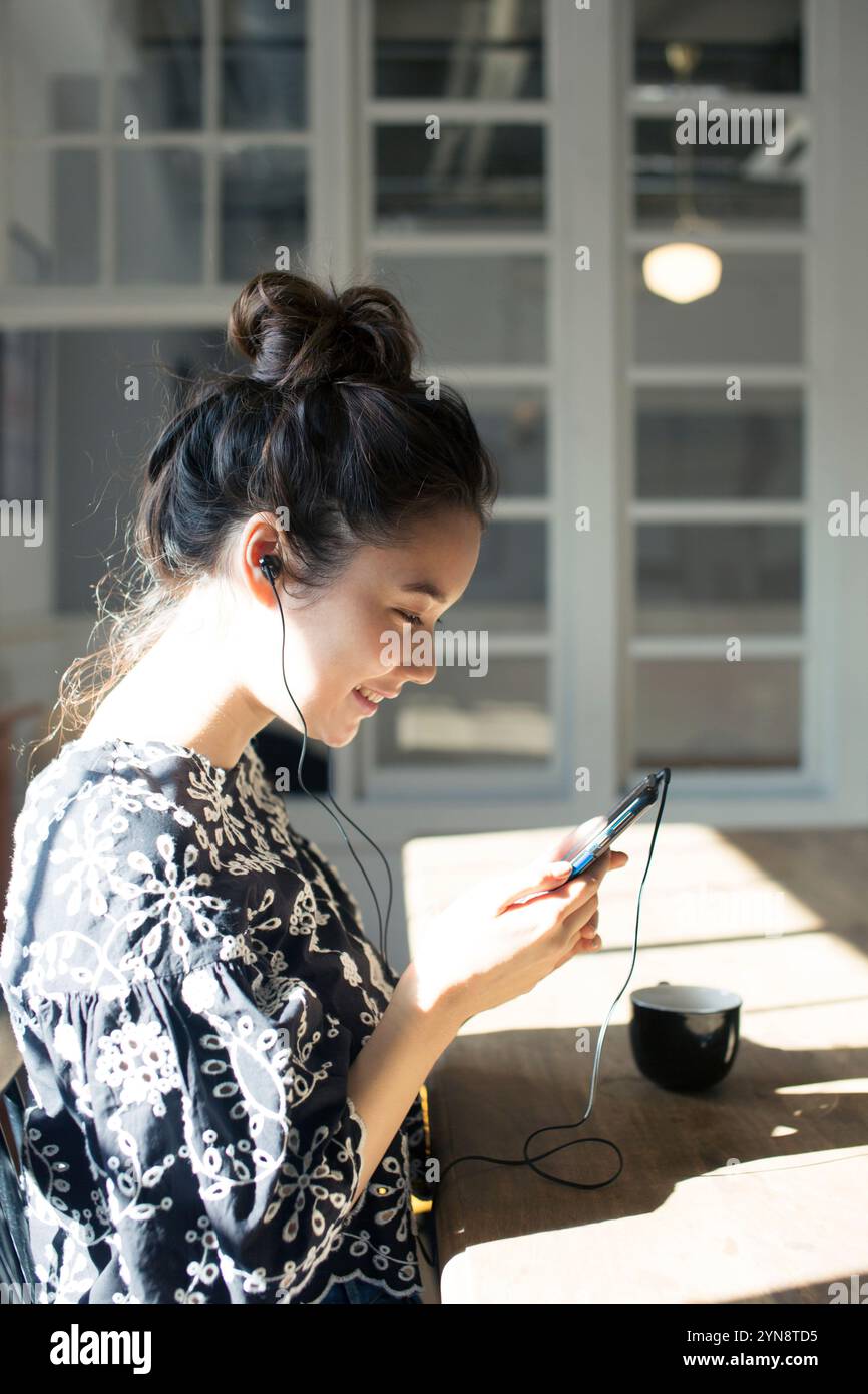 Woman in her 20s sitting by the window looking at her phone Stock Photo ...