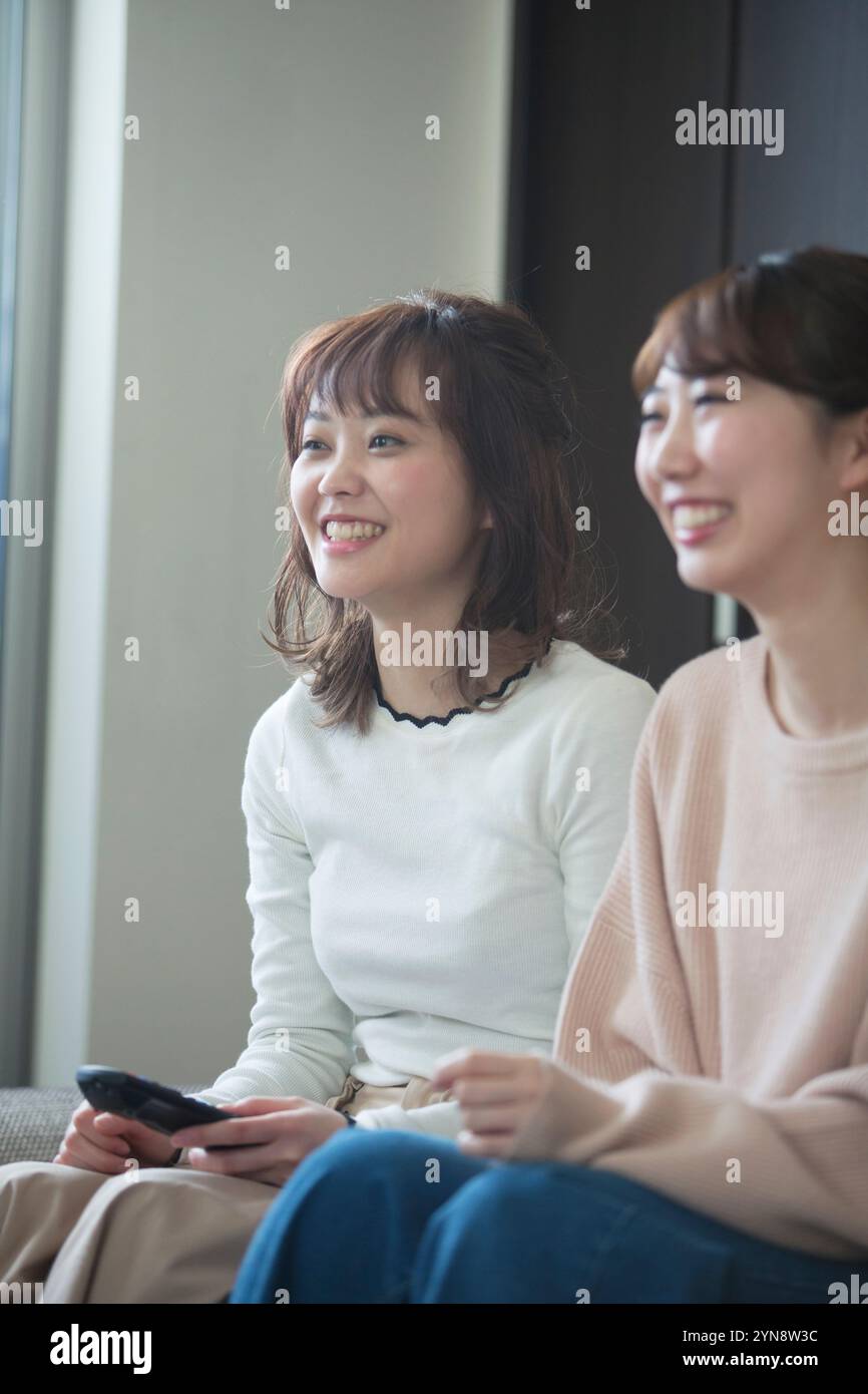 Two smiling women in their 20s watching TV Stock Photo - Alamy